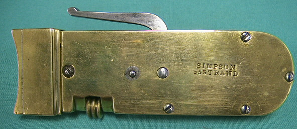 Rare form spring lancet marked with the Simpson mark and the 55 Strand address.  The instrument is armed by pulling the handle back to a half point that allos depth adjustment wiht the turn screw on the side.  After the depth has been set the arm is pulled all t he way back rotating the blade into an armed position.  The handle drops back into the starting position and is released by depressing the handle while holding the instrument with a "pen" grip.