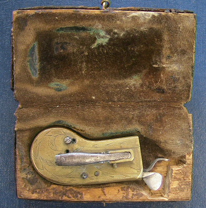 Very unusual English cased brass spring lancet with ornate floral engraving c.1800-1825.  The piece is unusual from the construction of a hinged case to allow access to the inner workings unlike the normal sliding groove design.  Another similar item in iron can be seen in the section or iron spring lancets.